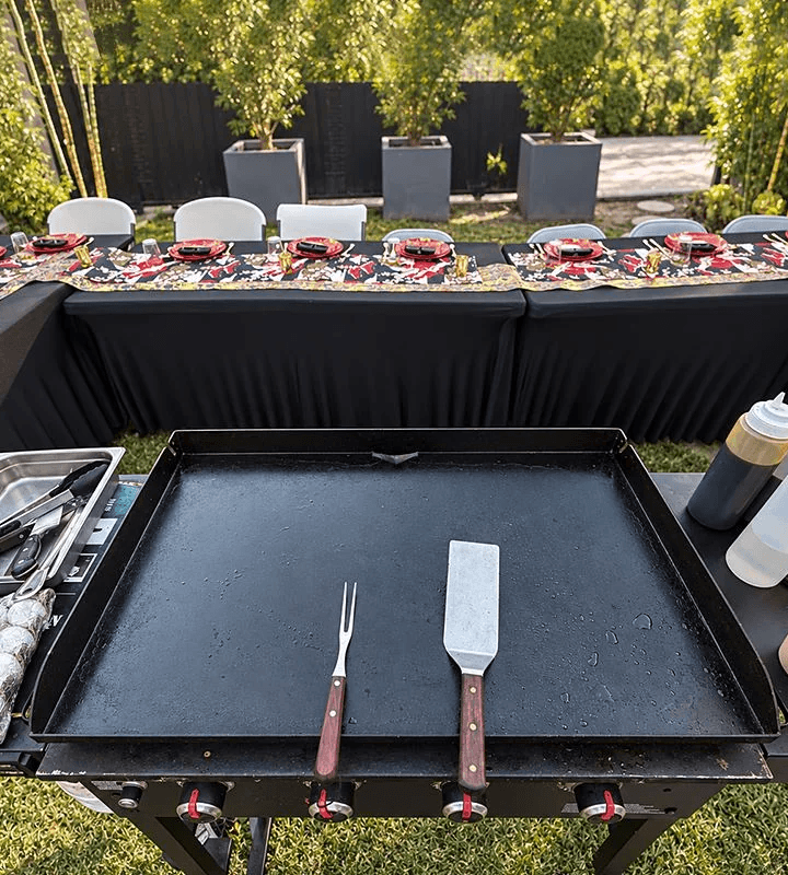 U-shaped outdoor dining setup beside a pool at sunset with string lights overhead